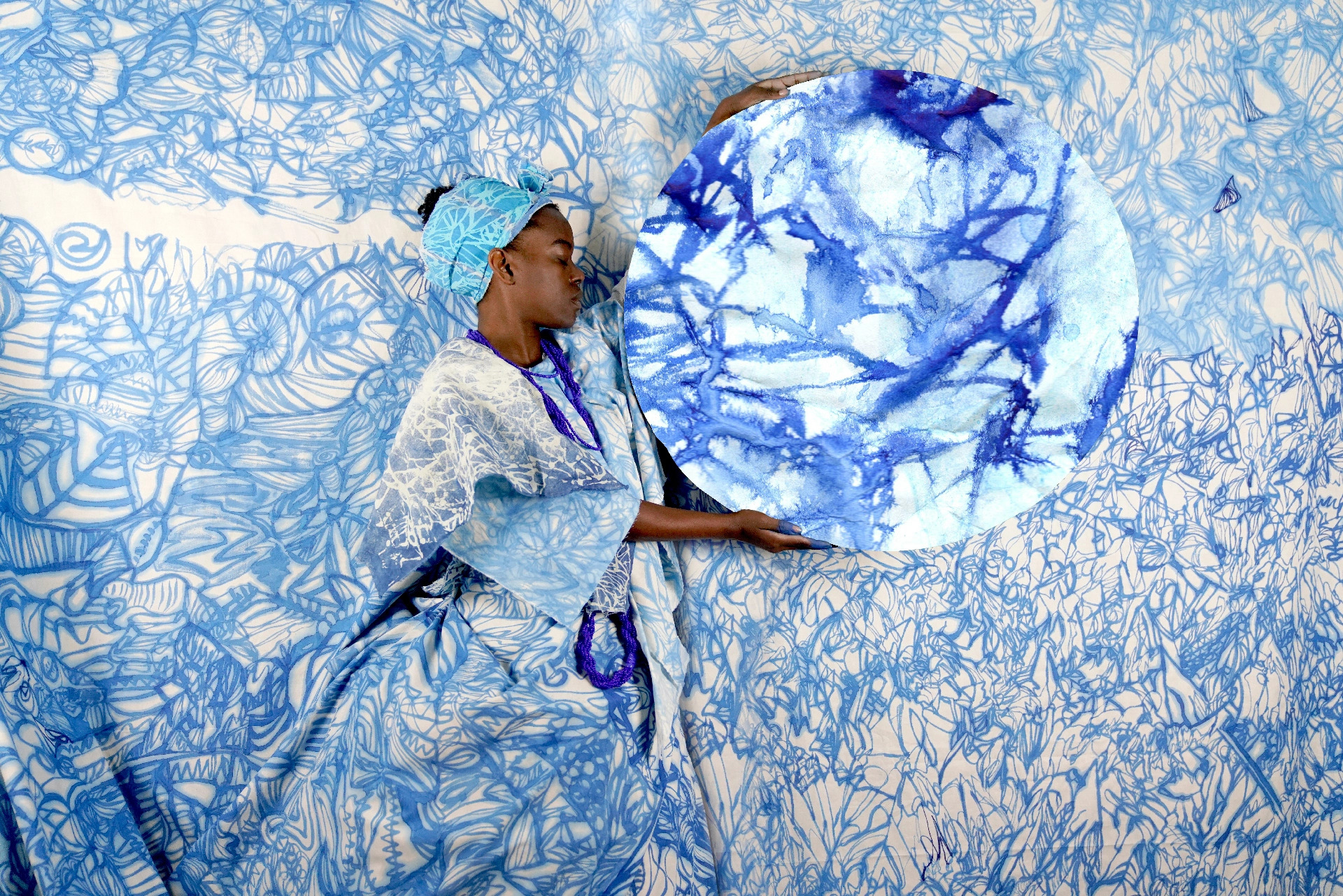 A black woman is represented holding a circle with white and blue patterns in her hands. The patterns are repeated across her dress and in the background