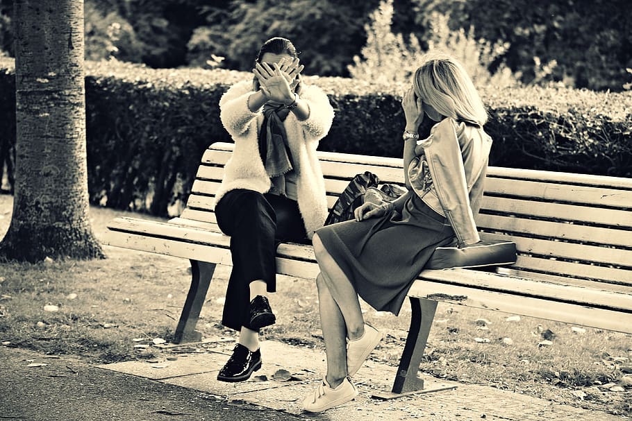 Two women on a bench, one putting her hands in front of her face
