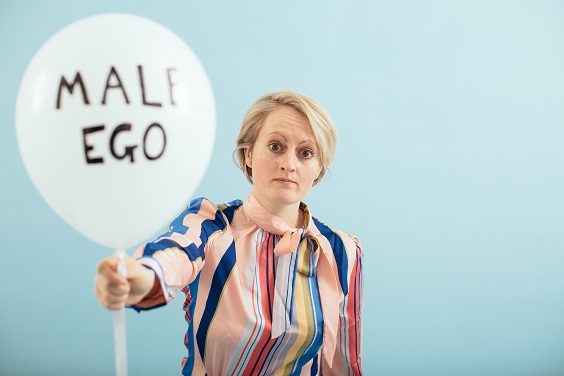 Melanie Jordan, who plays Andrea, holds a balloon with the words 'Male Ego' on it.