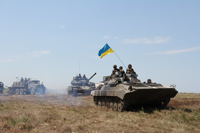 Military tanks driving through a field, with soldiers waving the Ukrainian flag