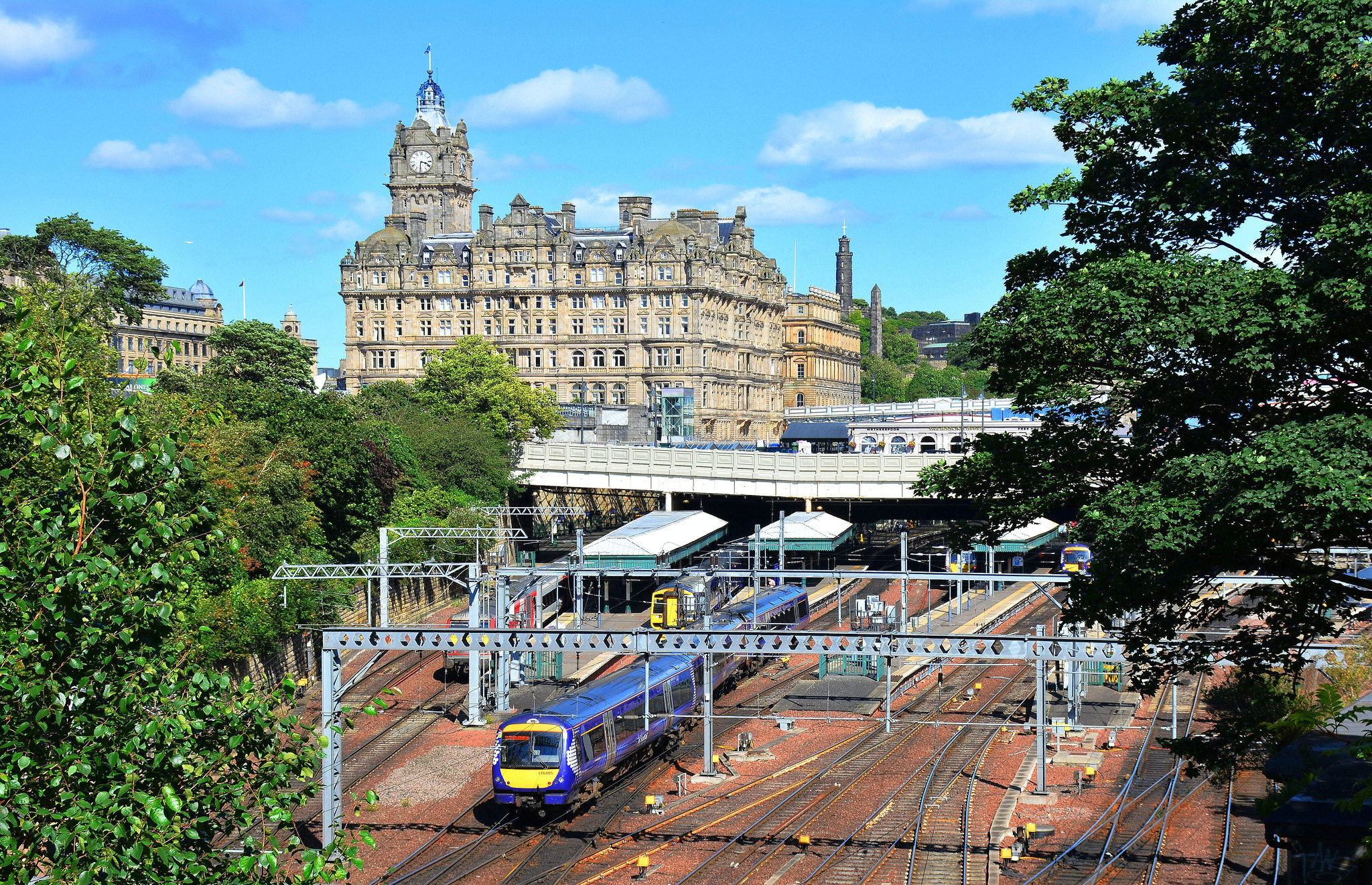 A view of Waverley Train Station from Princes Street gardens. A train can be seen leaving the station. Also in view is the Balmoral hotel on North Bridge.