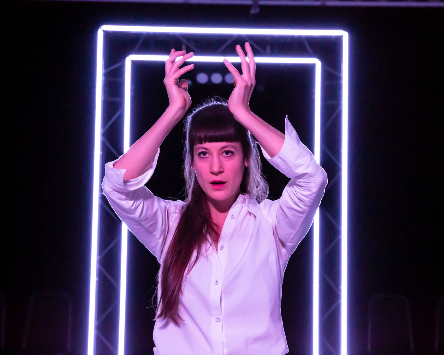 The actress of Antigone holding her hands up in front of some led doors