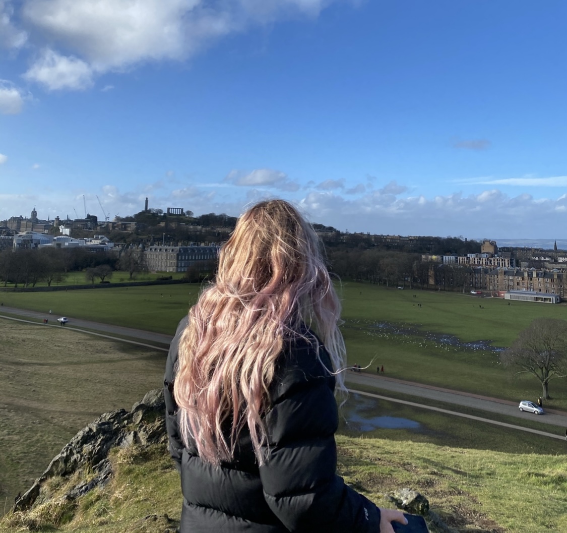 picture of blonde girl with back to camera outlooking the meadows on a clear blue day.