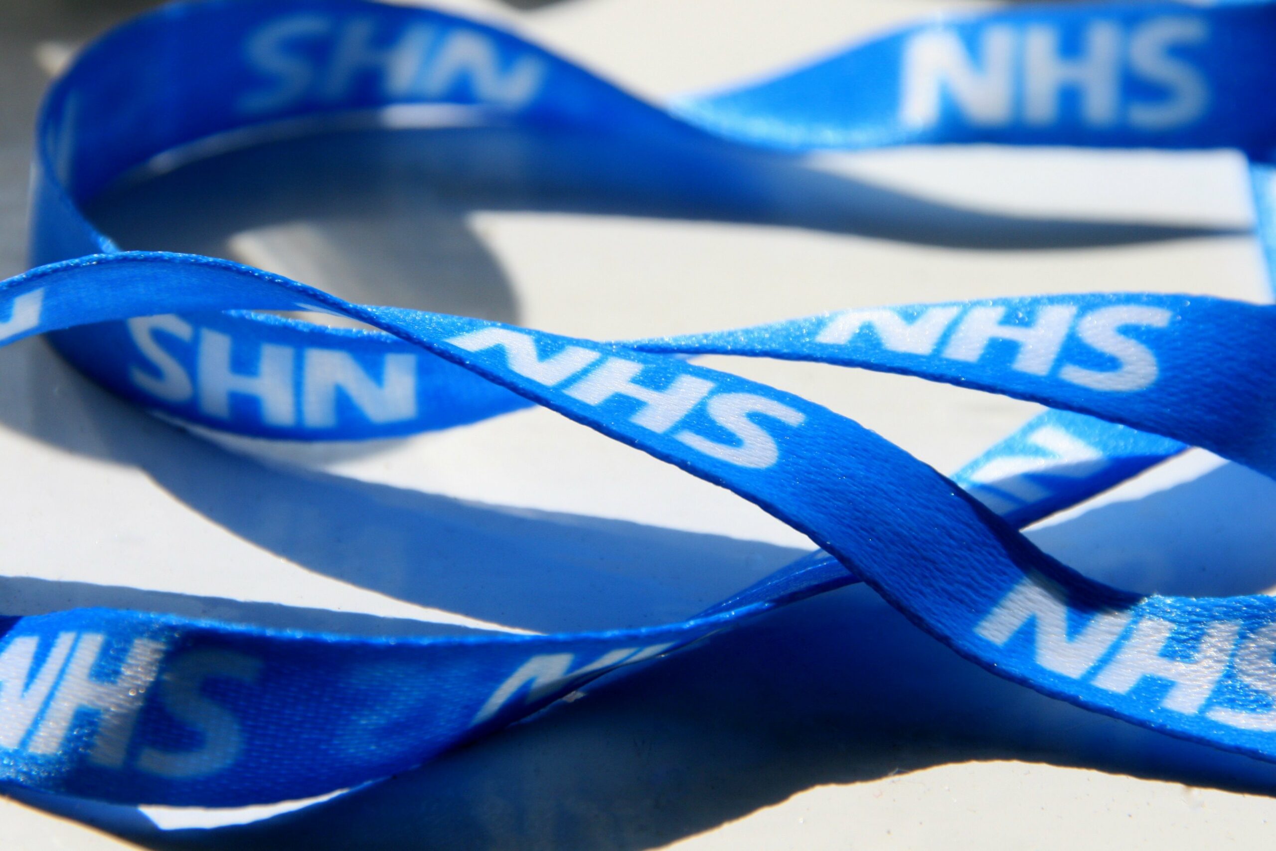 A blue lanyard with NHS printed on it laying on a grey table