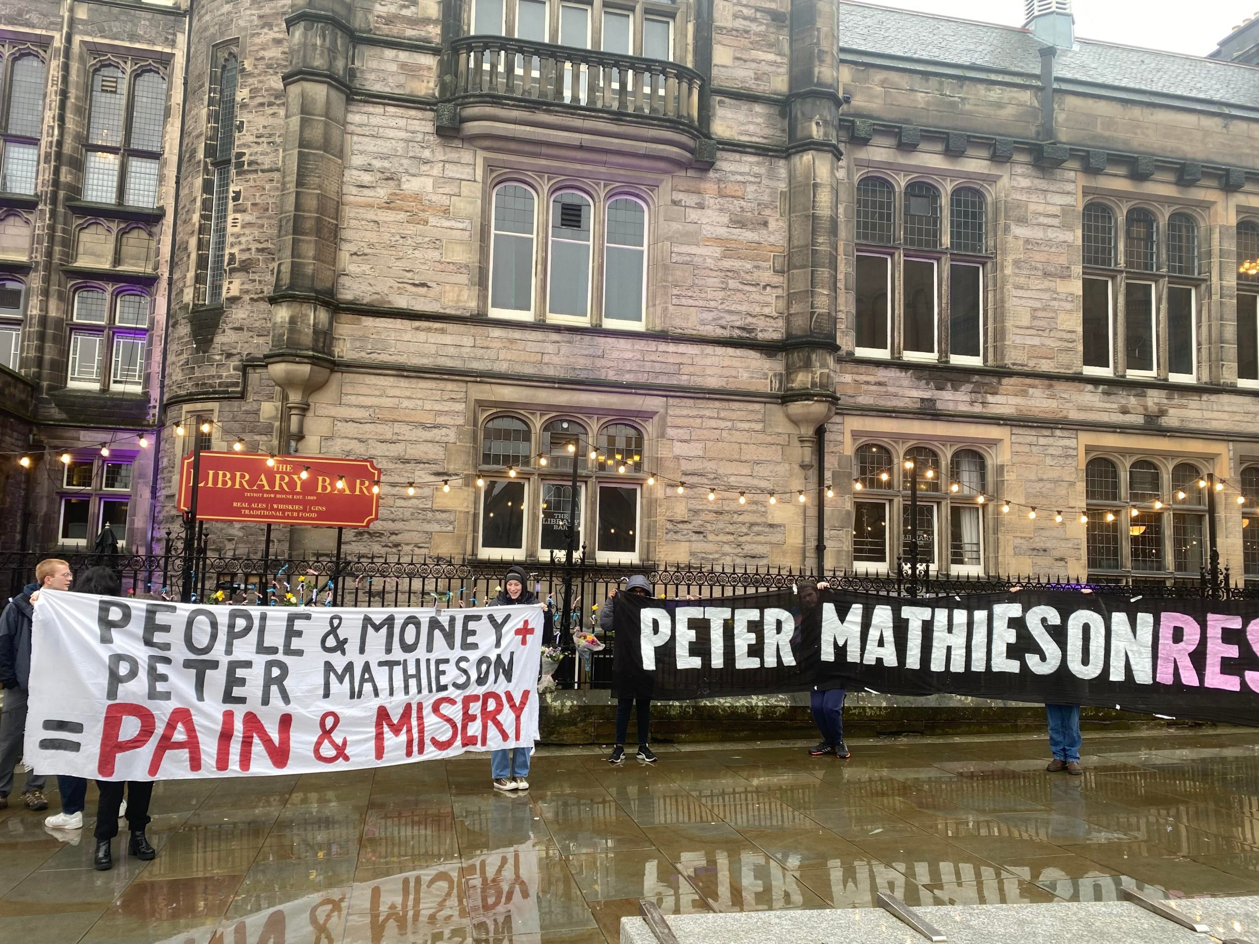 Several banners criticising University of Edinburgh principal and vice-chancellor Peter Mathieson in front of a brick, old students' union building