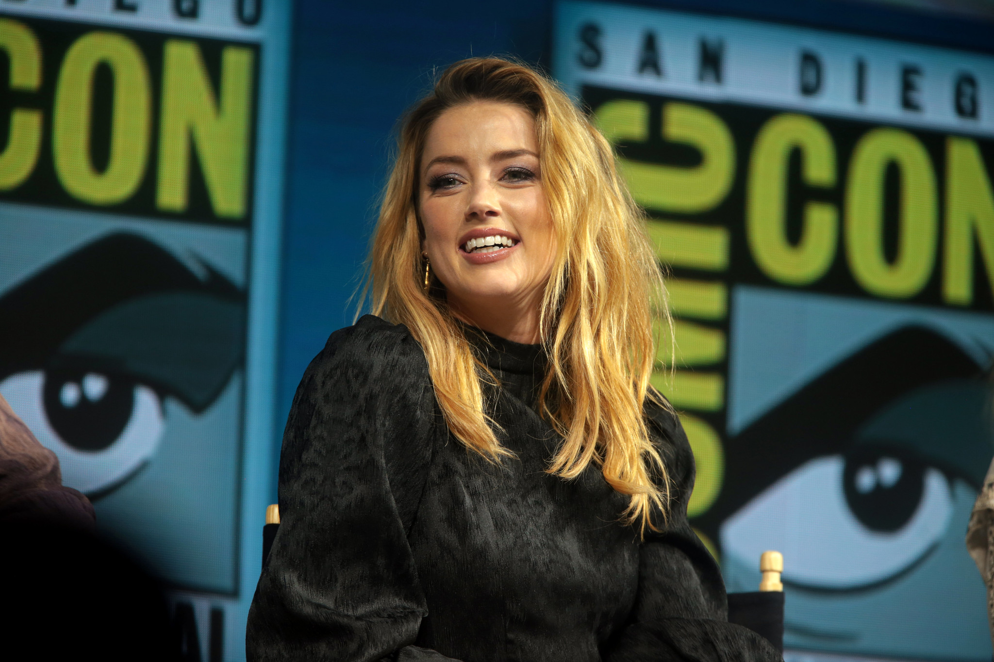 Amber Heard at San Diego Comic Con. She is on a panel and is smiling at the audience.