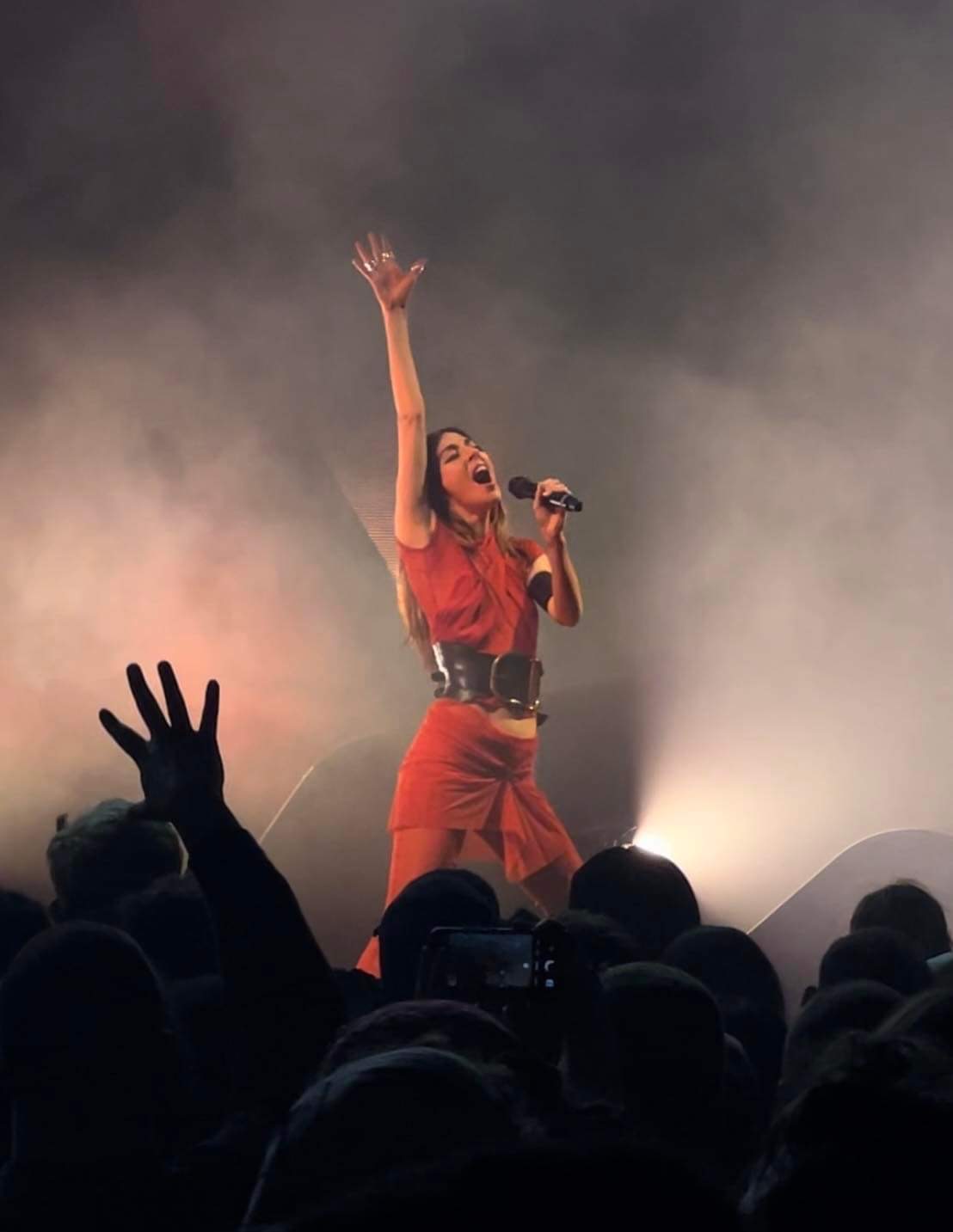 An image of Caroline with her hand in the air on stage in front of a crowd