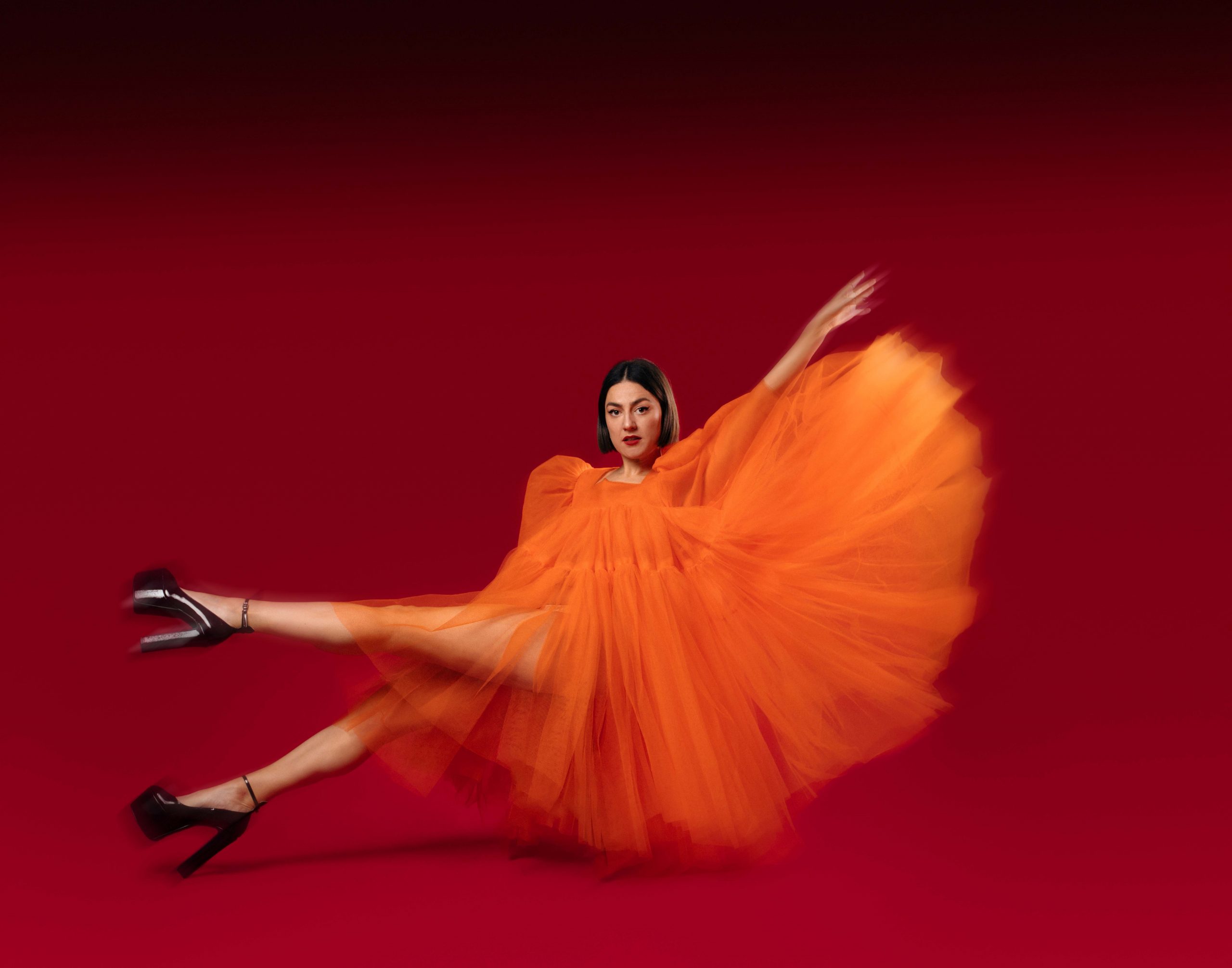 Tamsyn Kelly wears a huge orange tulle dress that fans out around her dramatically.