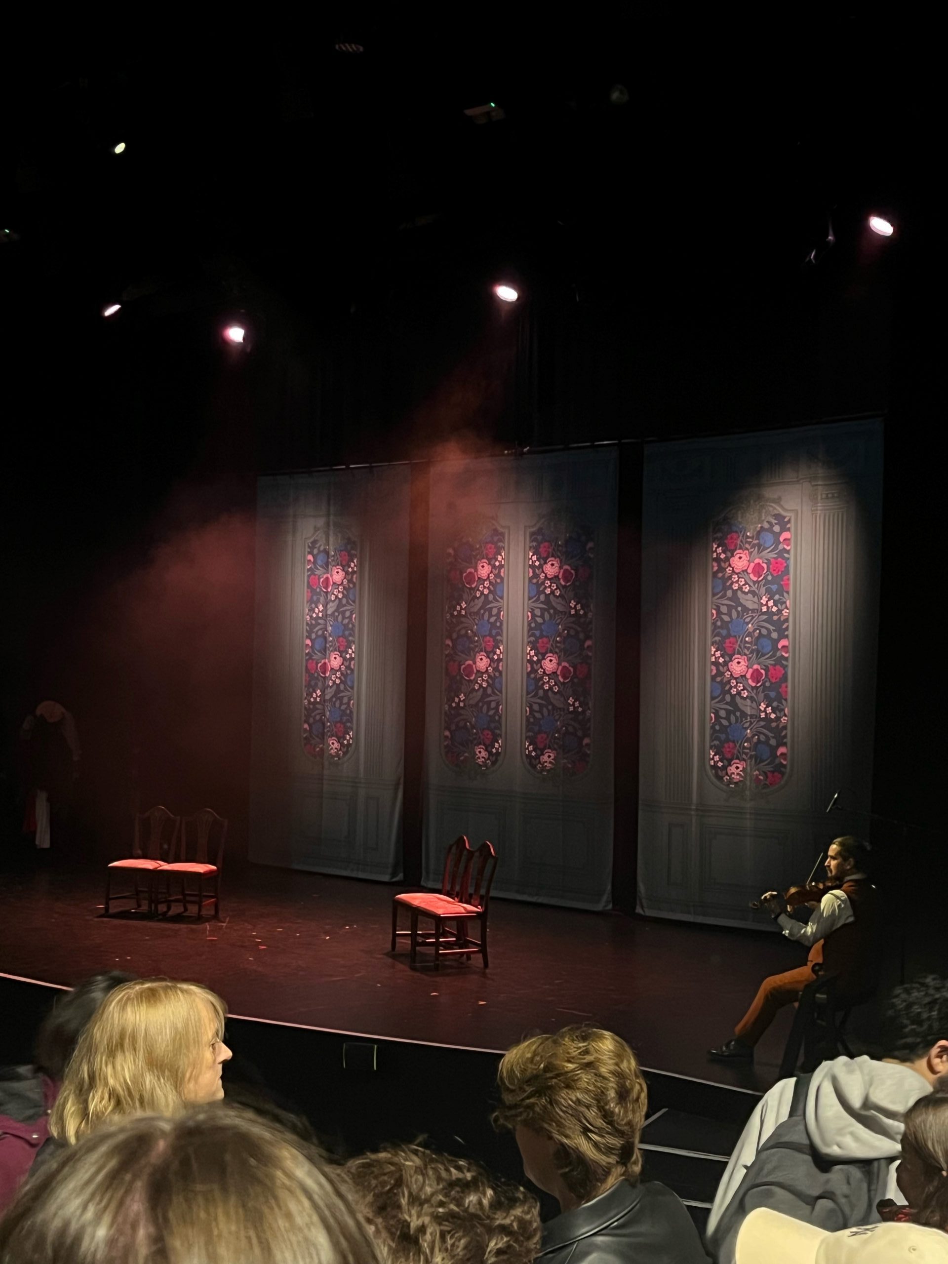 An empty stage with painted windows on the backdrop and a violinist in the corner