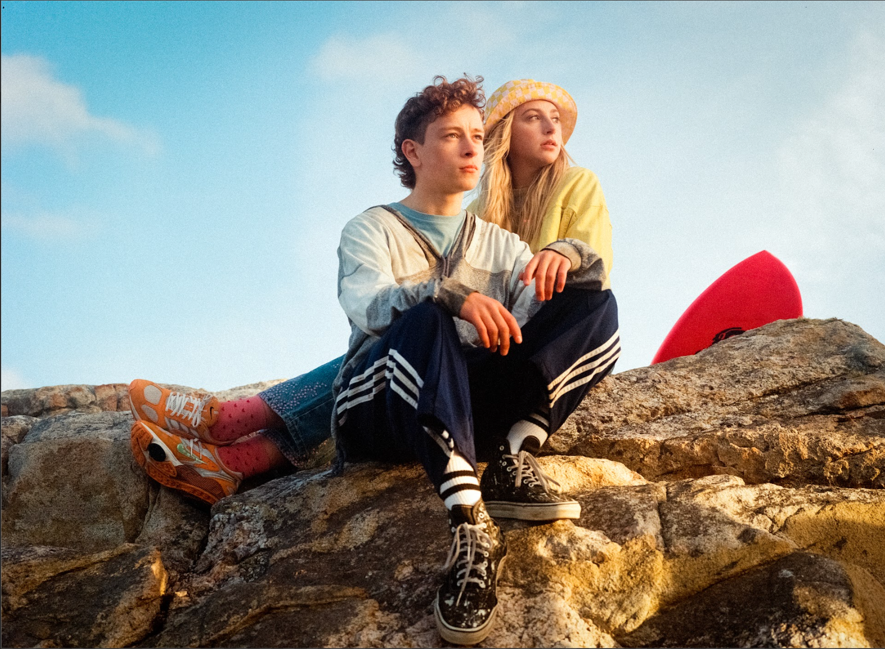 A young boy and a girl sit together on a rocky landscape against a blue sky.