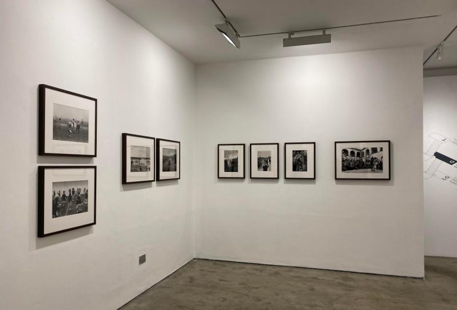 An image of an art gallery, on the centre of each wall is a selection of small black and white photographs in a row.