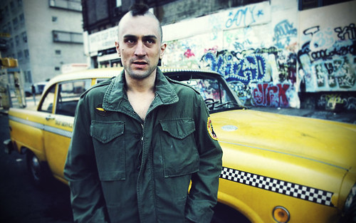 Taxi Driver star, Robert De Niro, poses in front of a taxi in character as Travis Bickle.