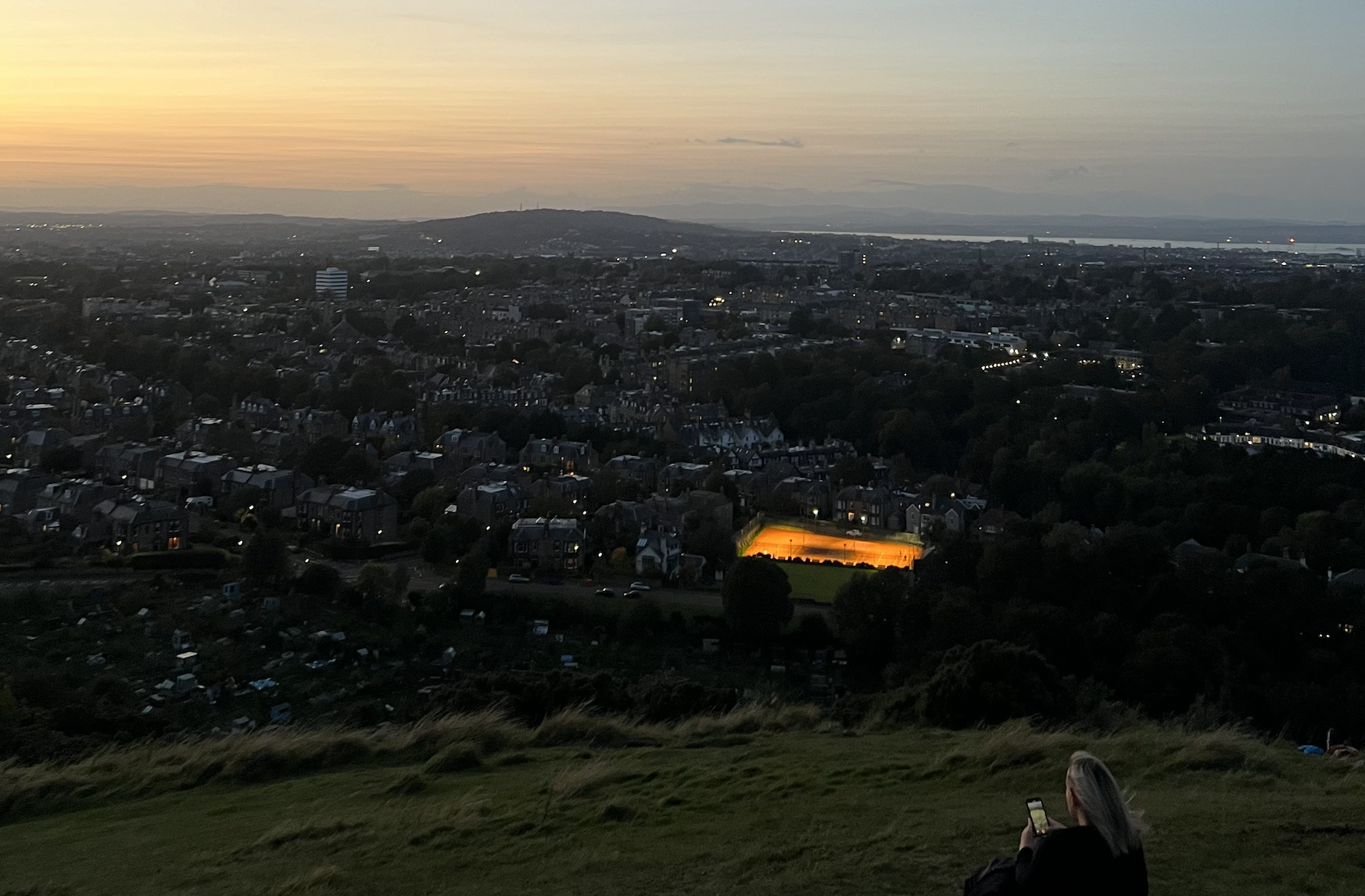 Edinburgh at night seen from Blackford Hill, woman sitting in front of the view