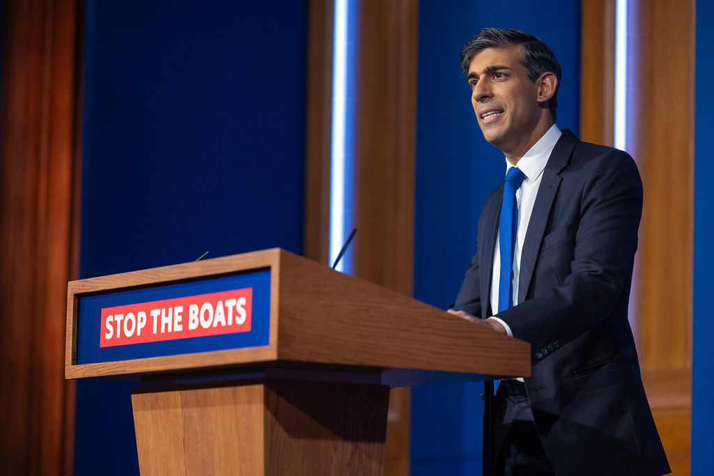A man in a suit giving a speech in front of sign which says stop the boats