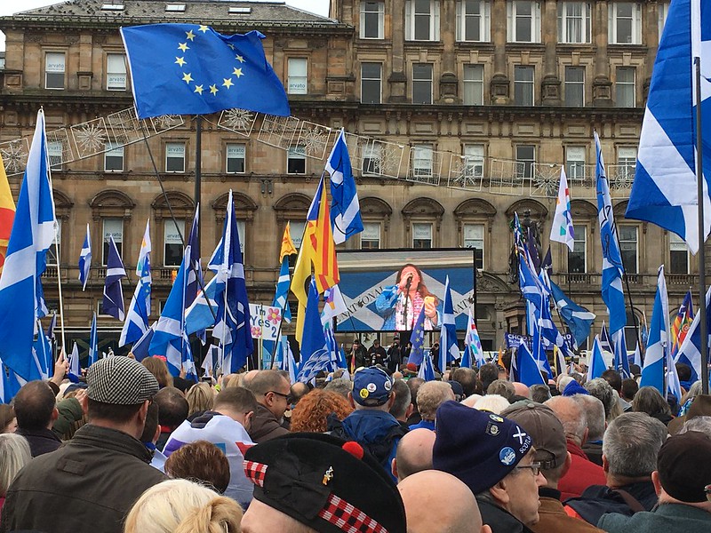 A crowd at a protest holding Scottish flags, EU flags, and Barcelona flags at a Yes movement rally