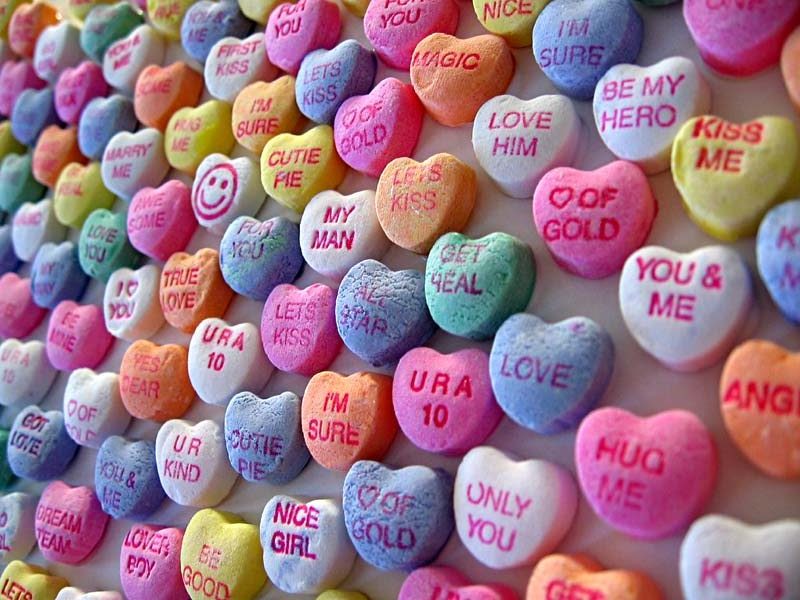 A variety of love heart sweets on a white background displaying romantic comments